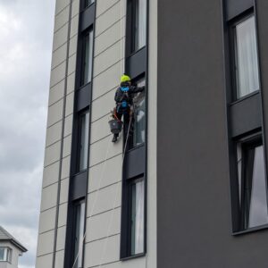 alpinista wyciera okno szmatką zwisając na linie